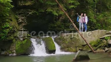 一对年轻的游客正站在山河上的瀑布附近。 欣赏美景.. 旅游业和旅游业
